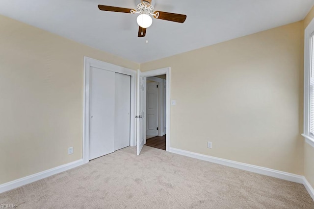 unfurnished bedroom featuring a closet, light colored carpet, ceiling fan, and baseboards