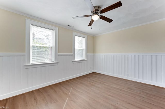 empty room with visible vents, ornamental molding, a wainscoted wall, and light wood-style flooring