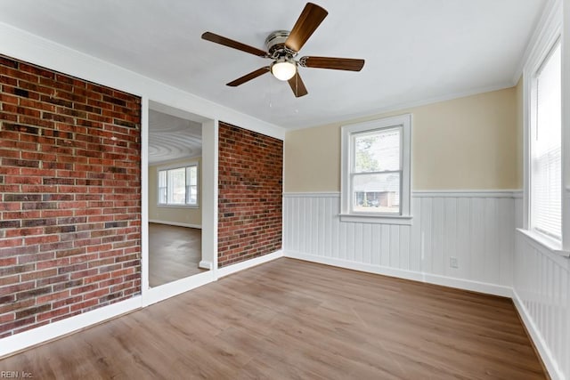 spare room with wainscoting, brick wall, ceiling fan, ornamental molding, and wood finished floors