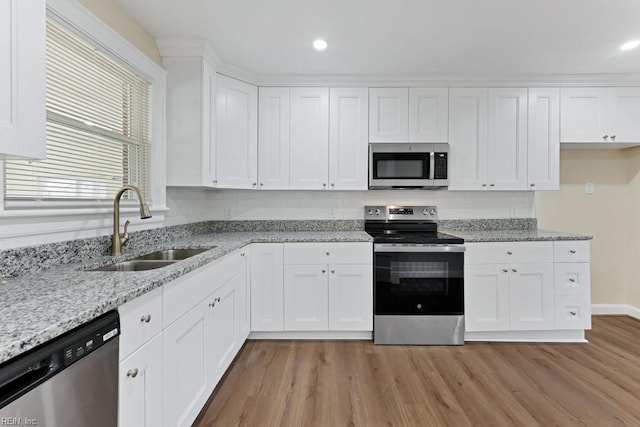 kitchen with appliances with stainless steel finishes, light wood-type flooring, a sink, and white cabinetry