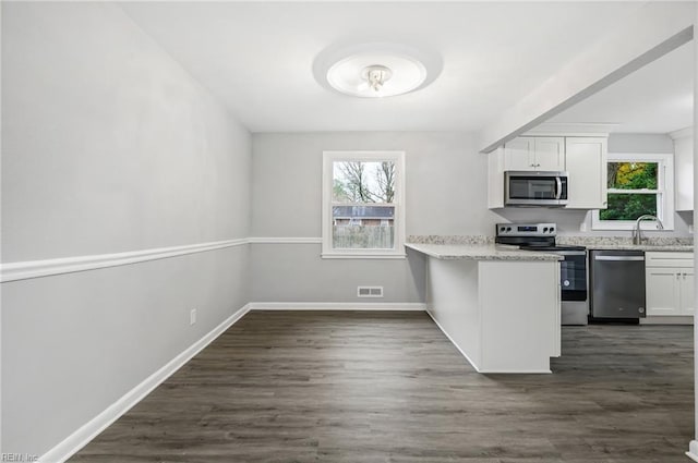 kitchen with white cabinets, appliances with stainless steel finishes, dark wood-type flooring, a peninsula, and light stone countertops