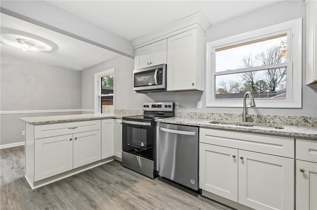 kitchen featuring stainless steel appliances, a peninsula, a sink, white cabinetry, and light stone countertops