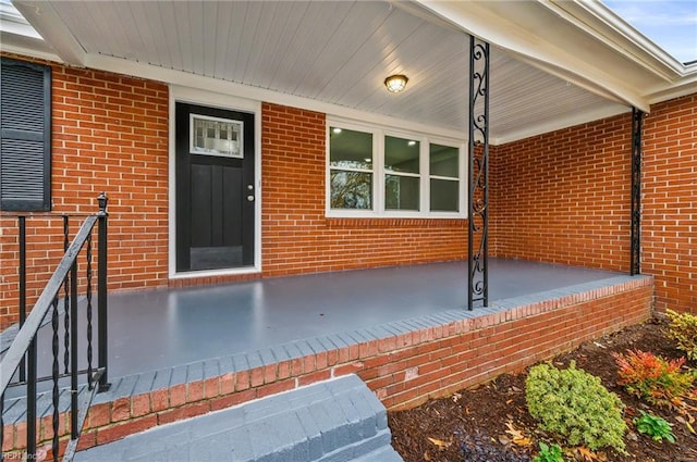 view of exterior entry featuring brick siding and a porch