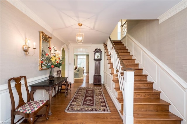 entryway featuring arched walkways, a decorative wall, stairway, ornamental molding, and wood finished floors