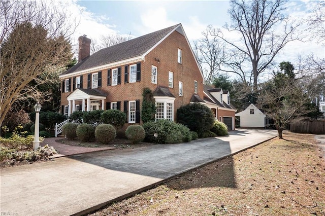 view of home's exterior featuring a garage, concrete driveway, brick siding, and a chimney