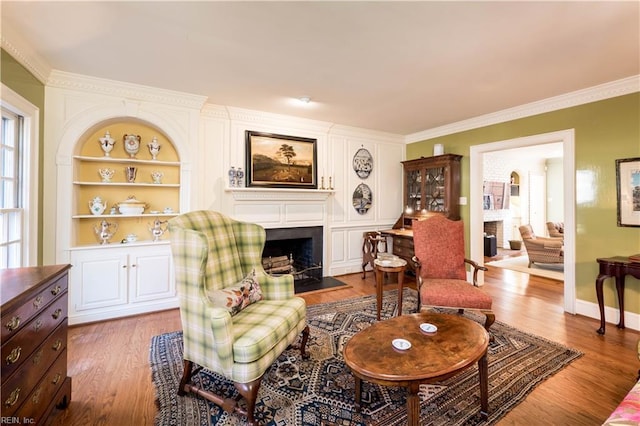 sitting room featuring a fireplace with flush hearth, built in features, wood finished floors, and ornamental molding