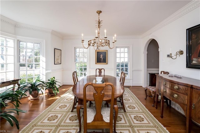 dining room featuring dark wood-style floors, arched walkways, a notable chandelier, and ornamental molding