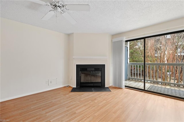 unfurnished living room with a fireplace with flush hearth, a ceiling fan, a textured ceiling, wood finished floors, and baseboards