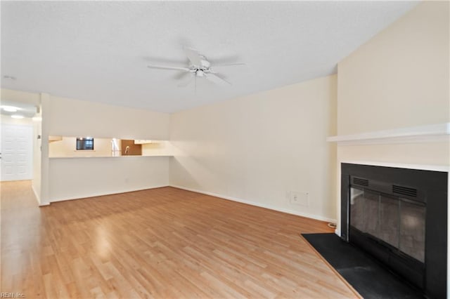 unfurnished living room with a fireplace with flush hearth, a ceiling fan, baseboards, and wood finished floors