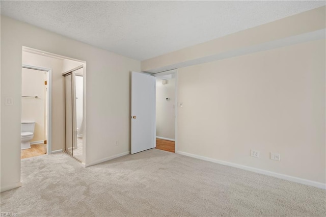 unfurnished bedroom featuring light carpet, a textured ceiling, and baseboards