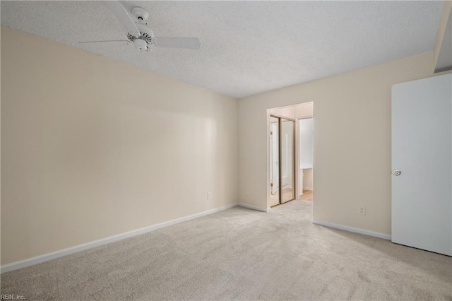 empty room with a ceiling fan, light colored carpet, a textured ceiling, and baseboards