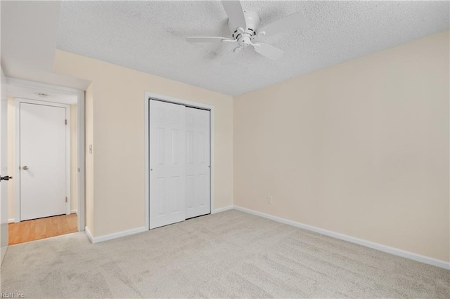 unfurnished bedroom featuring light carpet, a closet, a textured ceiling, and baseboards