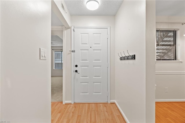 entryway featuring a textured ceiling, wood finished floors, visible vents, and baseboards