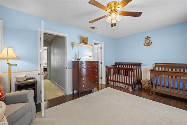 bedroom featuring a textured ceiling, dark wood-style flooring, visible vents, and a ceiling fan