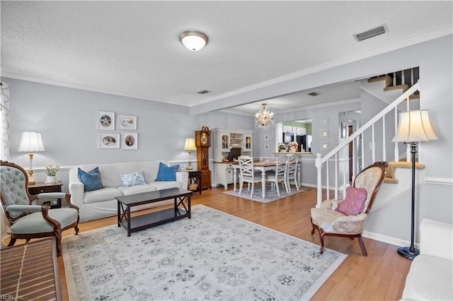 living area featuring a textured ceiling, wood finished floors, visible vents, stairs, and crown molding