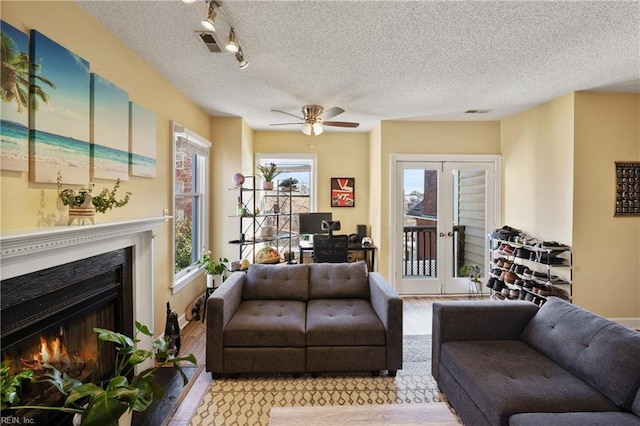 living room with a warm lit fireplace, light wood finished floors, a textured ceiling, and french doors