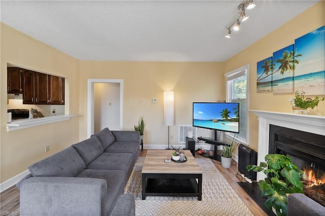 living area with a warm lit fireplace, light wood finished floors, visible vents, and baseboards