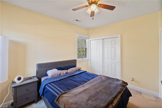 bedroom with a textured ceiling, light colored carpet, visible vents, baseboards, and a closet