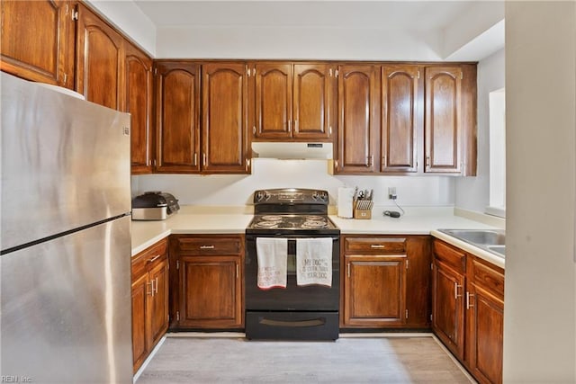 kitchen with brown cabinets, freestanding refrigerator, light countertops, black electric range, and under cabinet range hood