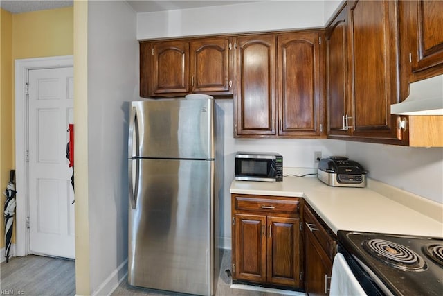 kitchen featuring under cabinet range hood, baseboards, stainless steel appliances, and light countertops