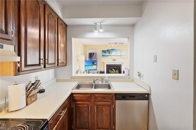 kitchen with under cabinet range hood, a fireplace, a sink, light countertops, and stainless steel dishwasher