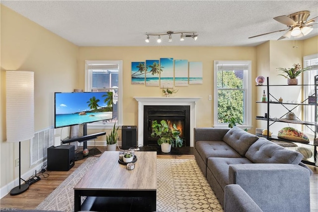 living room with visible vents, light wood-style flooring, a fireplace with flush hearth, a ceiling fan, and a textured ceiling