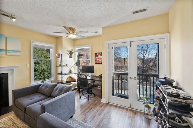 interior space featuring french doors, a fireplace, light wood finished floors, visible vents, and a textured ceiling