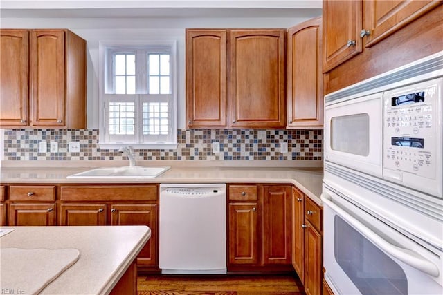 kitchen featuring white appliances, decorative backsplash, light countertops, and a sink