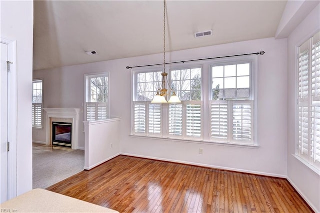 unfurnished dining area featuring hardwood / wood-style floors, a fireplace with flush hearth, visible vents, and baseboards