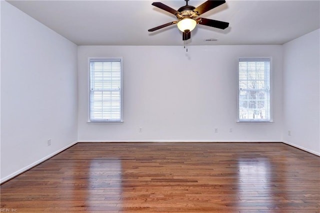 spare room featuring baseboards, dark wood-type flooring, visible vents, and a ceiling fan