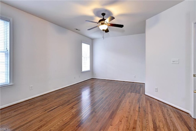 empty room featuring plenty of natural light, ceiling fan, and dark wood-type flooring