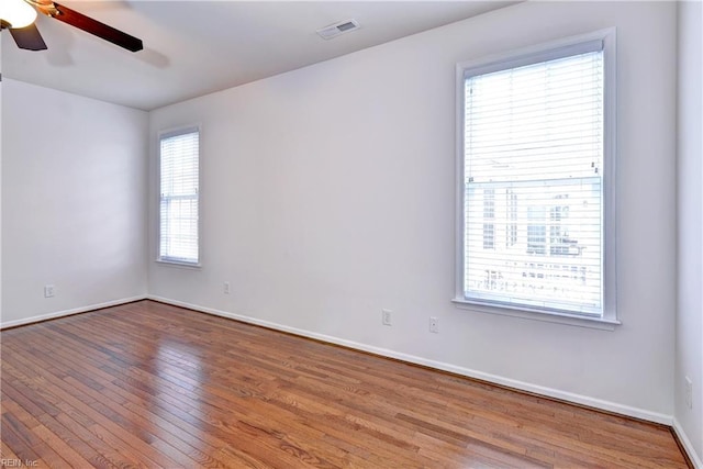 unfurnished room with ceiling fan, wood-type flooring, visible vents, and baseboards