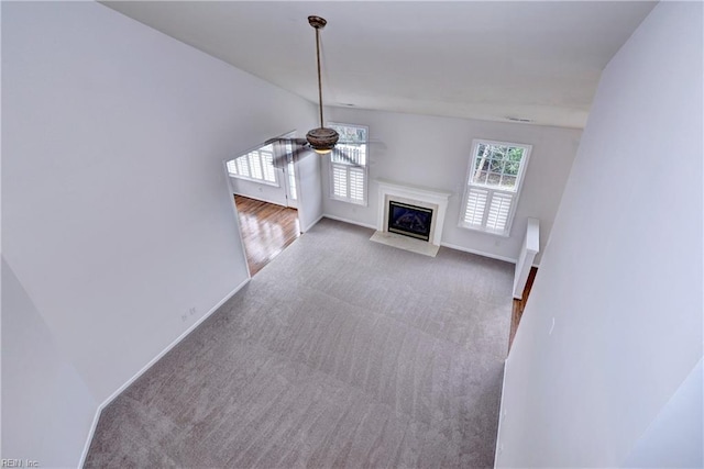 unfurnished living room featuring a ceiling fan, a high end fireplace, light colored carpet, and baseboards