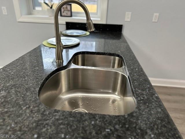 room details with baseboards, a sink, dark stone countertops, and wood finished floors