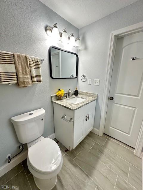 bathroom featuring toilet, baseboards, a textured ceiling, and vanity