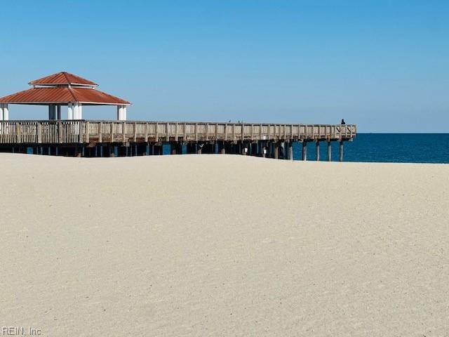 view of dock with a pier, a water view, and a view of the beach