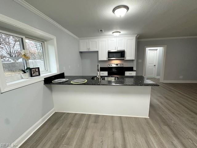 kitchen featuring appliances with stainless steel finishes, ornamental molding, white cabinets, a sink, and wood finished floors