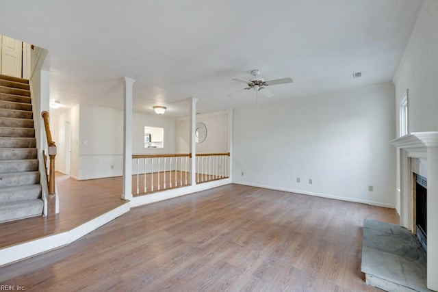 unfurnished living room featuring a wealth of natural light, a fireplace with raised hearth, stairway, light wood-style flooring, and a ceiling fan