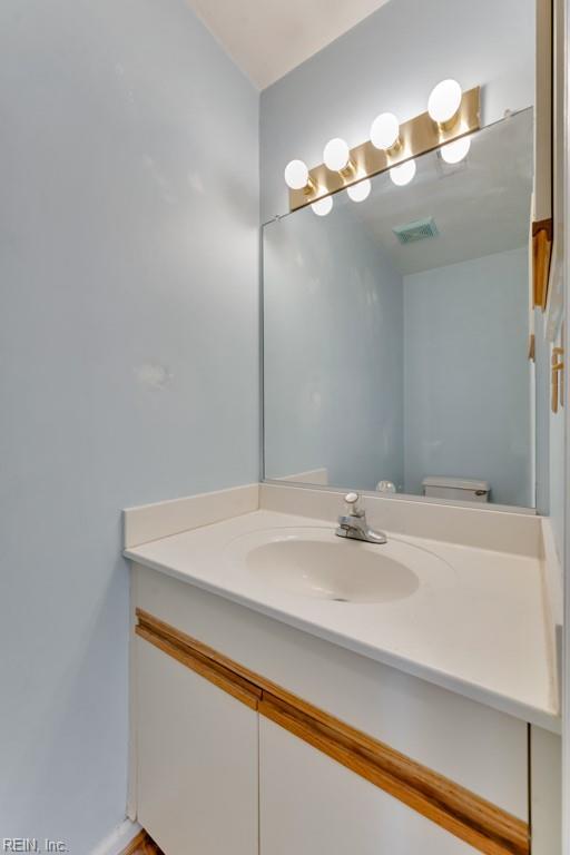 half bath with toilet, vanity, and visible vents