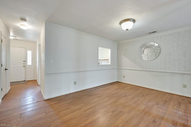 empty room with baseboards, visible vents, crown molding, and light wood finished floors