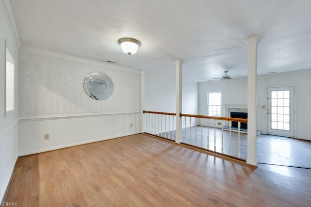 empty room with ornamental molding, light wood finished floors, a fireplace, and a ceiling fan