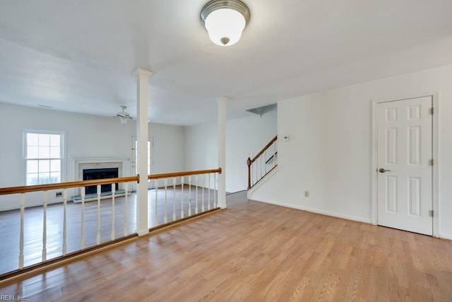 empty room featuring ceiling fan, a fireplace, light wood-style floors, stairs, and ornate columns