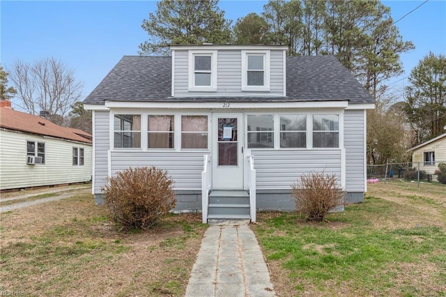 bungalow-style home featuring entry steps, a front lawn, roof with shingles, and fence