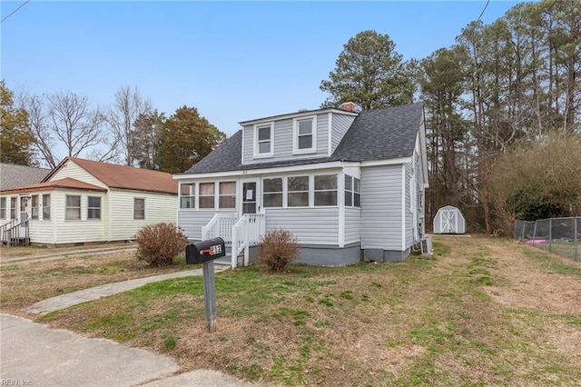 bungalow-style home with a front yard, roof with shingles, an outdoor structure, and a storage unit