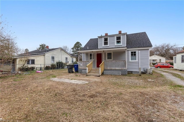 view of front of home featuring a porch, fence, roof with shingles, a chimney, and a front yard