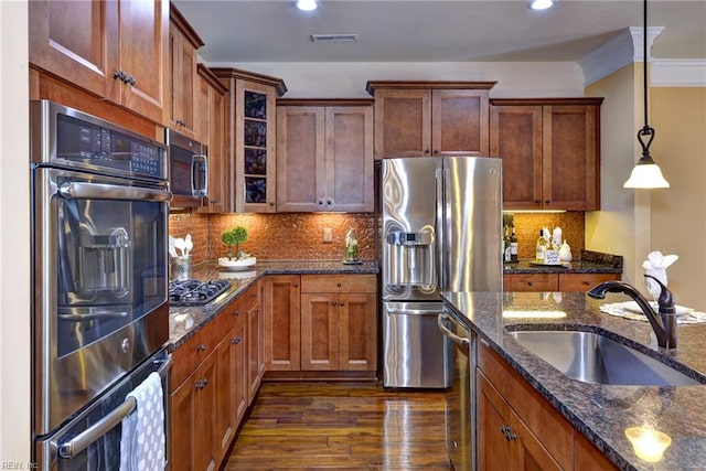 kitchen with glass insert cabinets, appliances with stainless steel finishes, dark stone countertops, hanging light fixtures, and a sink