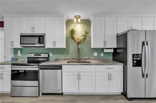 kitchen featuring tasteful backsplash, white cabinets, light wood-style flooring, stainless steel appliances, and a sink