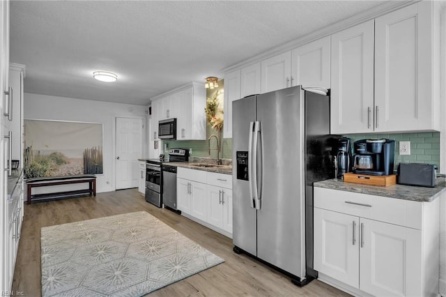 kitchen featuring appliances with stainless steel finishes, white cabinets, a sink, and light wood finished floors