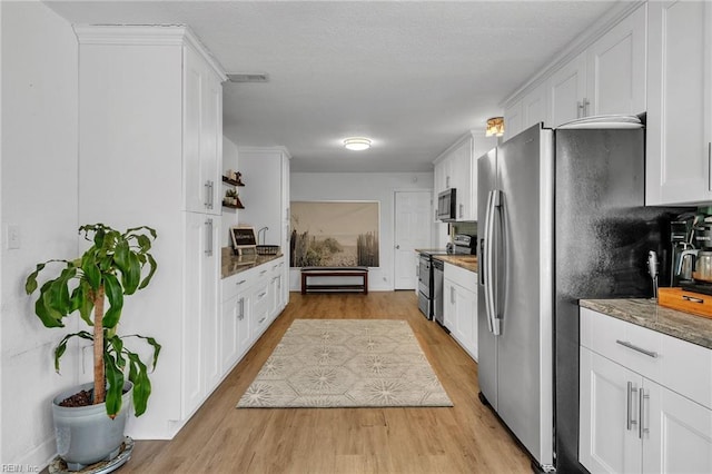 kitchen featuring dark stone counters, stainless steel appliances, white cabinetry, and light wood-style floors