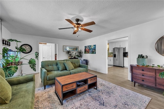 living area with ceiling fan, a textured ceiling, and light wood-style floors